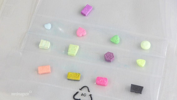 Mehrere Ecstasy-Tabletten liegen in bunten Farben auf einem Tisch. © Screenshot 