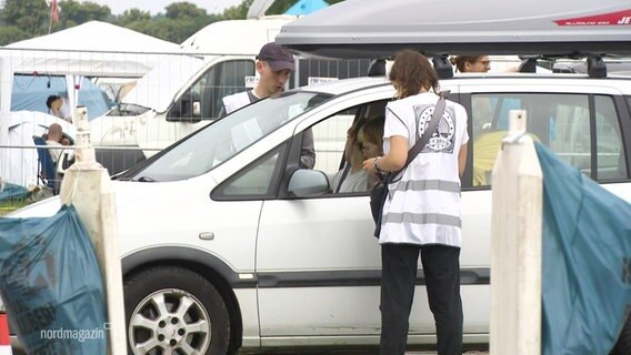 Zwei Mitarbeiter des Festival-Personals kontrollieren ein Auto, das auf das Gelände auffahren will. © Screenshot 