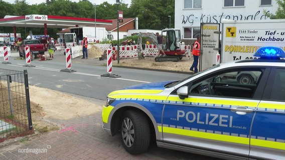 Ein Polizeiauto steht am Rand einer Straße auf der eine Spur wegen einer Baustelle vor einer Tankstelle gesperrt ist. © Screenshot 