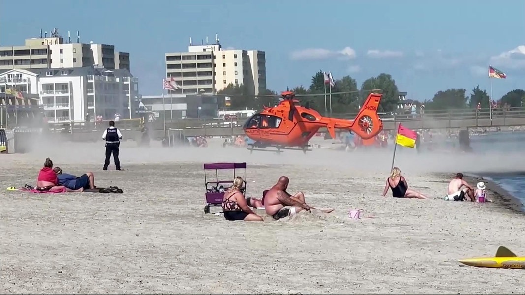 Ein Rettungshubschrauber landet an einem Badestrand. Dabei wirbelt er sehr viel Sand auf.
