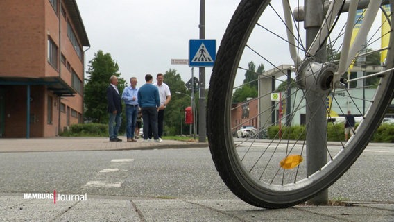 Im Vordergrund steht ein Fahrrad, dahinter dikutieren Gewerbetreibende über eine geplante Fahrradstraße. © Screenshot 
