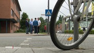Im Vordergrund steht ein Fahrrad, dahinter dikutieren Gewerbetreibende über eine geplante Fahrradstraße. © Screenshot 