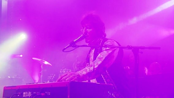 Singender Keyboarder in lila getauchtes Licht. © Screenshot 