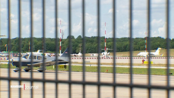 Durch einen Zaun erkennt man einen Flughafen mit Privatjets. © Screenshot 