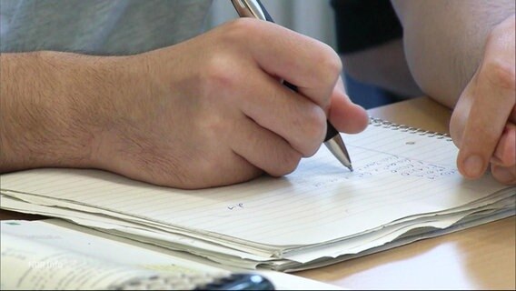 Nahaufnahme einer mit einem Kugelschreiber auf einen Block schreibende Hand. © Screenshot 