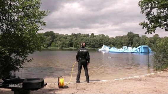 Ein Polizist steht am Ufer eines Sees. © Screenshot 