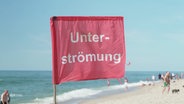 Eine rote Flagge an einem Strand warnt vor Unterströmungen. © Screenshot 