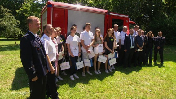 Die jungen Feuerwehrleute vor einem Feuerwehrauto aufgereiht. © Screenshot 