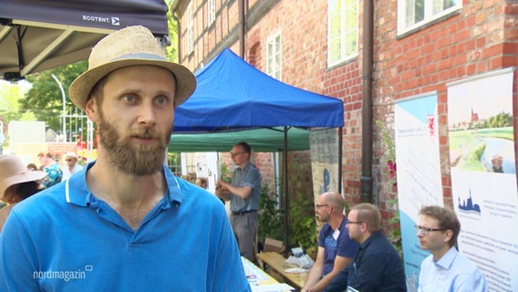 Ein Mann mit beigem Hut und blauem T-Shirt. © Screenshot 