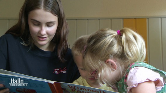 Eine junge Frau liest Kindern aus einem Buch vor. © Screenshot 