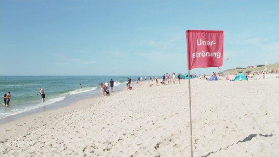Eine rote Fahne weht an einem Strand, sie trägt die Aufschrift: "Unterströmung". © Screenshot 