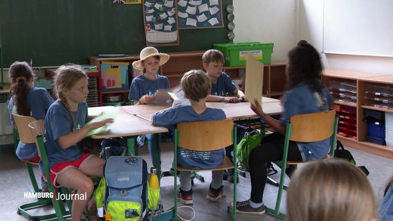 Kinder sitzend an einem Tisch in einer Schule © Screenshot 