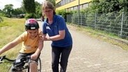 Eine Frau stützt ein kind beim Fahrradfahren. © Screenshot 