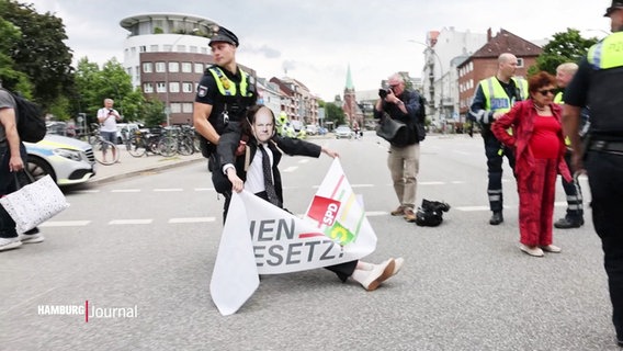 Poliezei trägt Person mit Maske und Plakat weg © Screenshot 