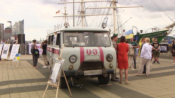 Ein zerschossener Krankenwagen aus der Ukraine wird auf der Jan-Fedder-Promenade in Hamburg ausgestellt. © Screenshot 