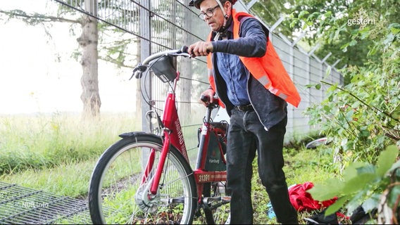 Person mit Warnweste und Fahrrad an einem Zaun © Screenshot 