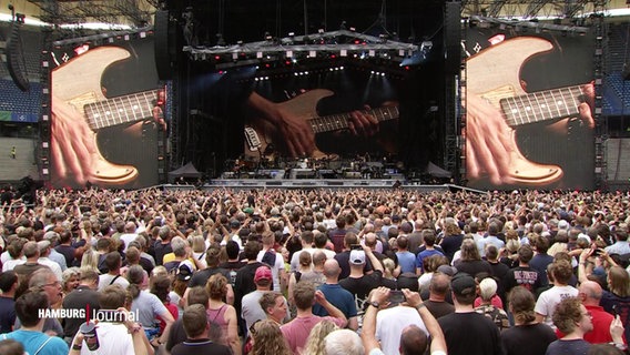 Zahlreiche Menschen stehen dicht an dicht vor einer Bühne, auf der Bruce Springsteen spielt. © Screenshot 