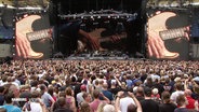 Zahlreiche Menschen stehen dicht an dicht vor einer Bühne, auf der Bruce Springsteen spielt. © Screenshot 