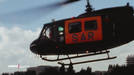 Ein Hubschrauber der Luftrettung. Er ist komplett schwarz, nur der Türbereich ist orange, darauf steht in dunklen Buchstaben "SAR". © Screenshot 