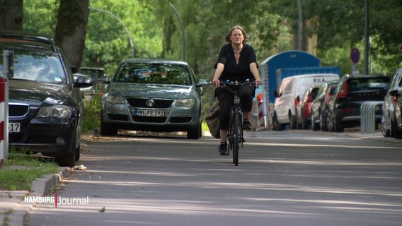 Eine Fahrradfahrerin fährt auf einer Straße, am Straßenrand parkende Autos. © Screenshot 