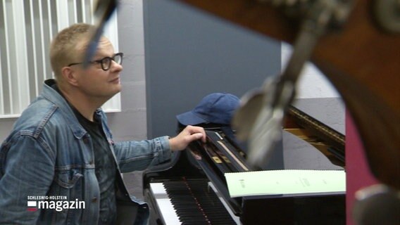 Pianist Iiro Rantala während einer Probe am Flügel, im Vordergrund unscharf die Umrisse der Wirbel eines Cellos. © Screenshot 