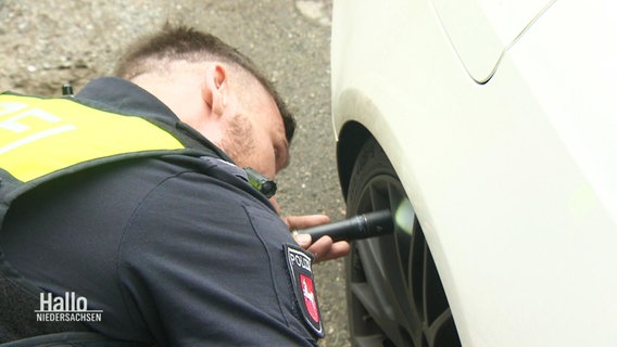 Ein Polizist untersucht den Radkasten eines Autos auf Drogen. © Screenshot 
