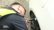 Ein Polizist untersucht den Radkasten eines Autos auf Drogen. © Screenshot 