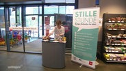 Eine Frau steht an einem Infodesk vor einem Plakat mit der Aufschrift "Stille Stunde". © Screenshot 