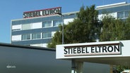 Ein Schild vor einem großen Gebäude zeigt die Aufschrift "Stiebel Eltron". © Screenshot 