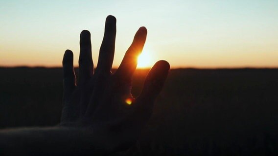 Eine ausgestreckte Hand im Gegenlicht vor einem SOnnenuntergang am Horizont. © Screenshot 