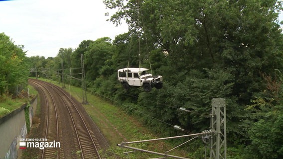 Ein Geländewagen hängt an einem Kran und wird aus eínem Gleisbett gehoben. © Screenshot 