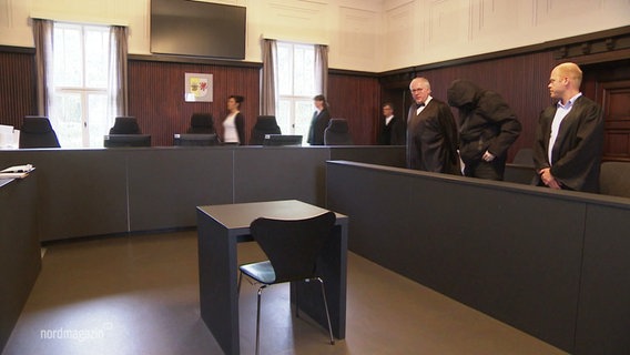 Angeklagter im Gerichtssaal, er verdeckt sein Gesicht mit einer FFP2-Maske und einer Kapuze. © Screenshot 