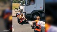 Ausschnitt eines Videos: EIn LKW fährt einen Aktivisten der "Letzten Generation" an, der auf einer Straße sitzt. © Screenshot 