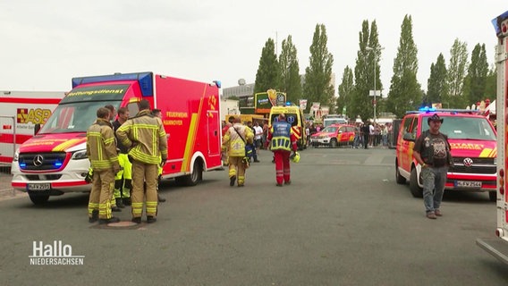 Auf einem größeren, asphaltierten Platz stehen mehrere Einsatzfahrzeuge von Feuerwehr und Rettungsdienst nach einem Unfall bei einer Autoshow. © Screenshot 