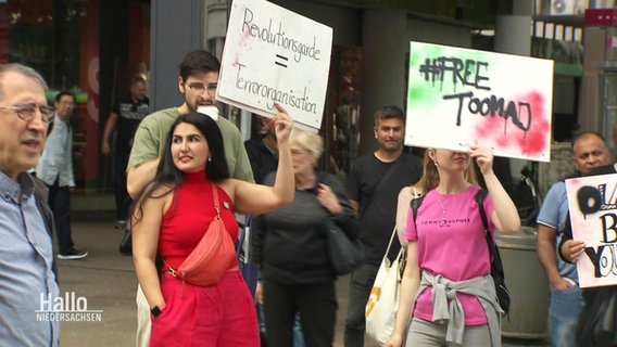 Bei einer Protestaktion halten mehrere Menschen Schilder mit Forderungen gegen das Regime im Iran empor. © Screenshot 