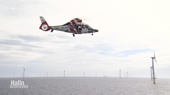 Ein Rettungshubschrauber schwebt über der Wasseroberfläche nahe einem Offshore-Windpark. © Screenshot 