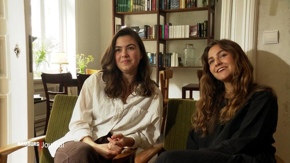 Zwei junge Frauen sitzen in Sesseln vor einem Bücherregal © Screenshot 