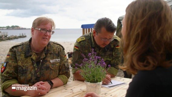 Eine Soldatin und ein Soldat in Uniform sitzen einer jungen Frau gegenüber © Screenshot 