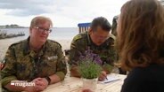 Eine Soldatin und ein Soldat in Uniform sitzen einer jungen Frau gegenüber © Screenshot 