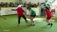 Jugendliche spielen auf einem kleinen Feld in einer Halle Fußball. © Screenshot 