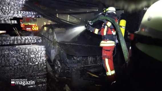Ein Feuerwehrmann löscht ein beinahe vollständig ausgebranntes Auto. © Screenshot 