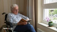 Eine ältere Dame sitzt an einem Fenster und liest ein Buch. © Screenshot 