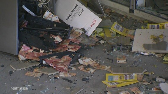 Auf einem verschmutzten Boden liegen mehrere verkohlte Banknoten vor einem aufgesprengten Bankautomaten. © Screenshot 