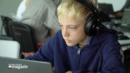 Ein Junge mit Kopfhörern hinter einem Laptop. © Screenshot 