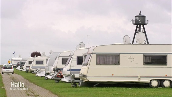Blick auf mehrere Camping-Wohnanhänger, die in einer Reihe auf dem Rasen eines Campingplatzes aufgestellt sind. © Screenshot 