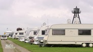 Blick auf mehrere Camping-Wohnanhänger, die in einer Reihe auf dem Rasen eines Campingplatzes aufgestellt sind. © Screenshot 