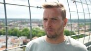 Der Trainer des Greifswalder FC, Lars Fuchs, im Interview auf einer Aussichtsplattform über einer Kleinstadt. © Screenshot 
