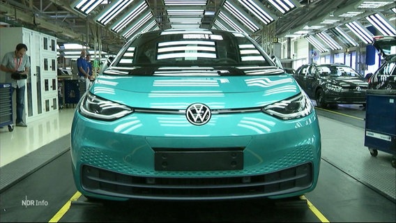 Ein türkis-glänzender Kleinwagen der Volkswagen-Marke steht auf einer Fabrikstraße in einer Werkhalle. © Screenshot 