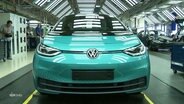 Ein türkis-glänzender Kleinwagen der Volkswagen-Marke steht auf einer Fabrikstraße in einer Werkhalle. © Screenshot 