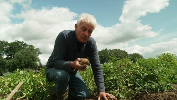 Ein Mann kniet in einem Feld und betrachtet eine Kartoffel, die er in der Hand hält. © Screenshot 